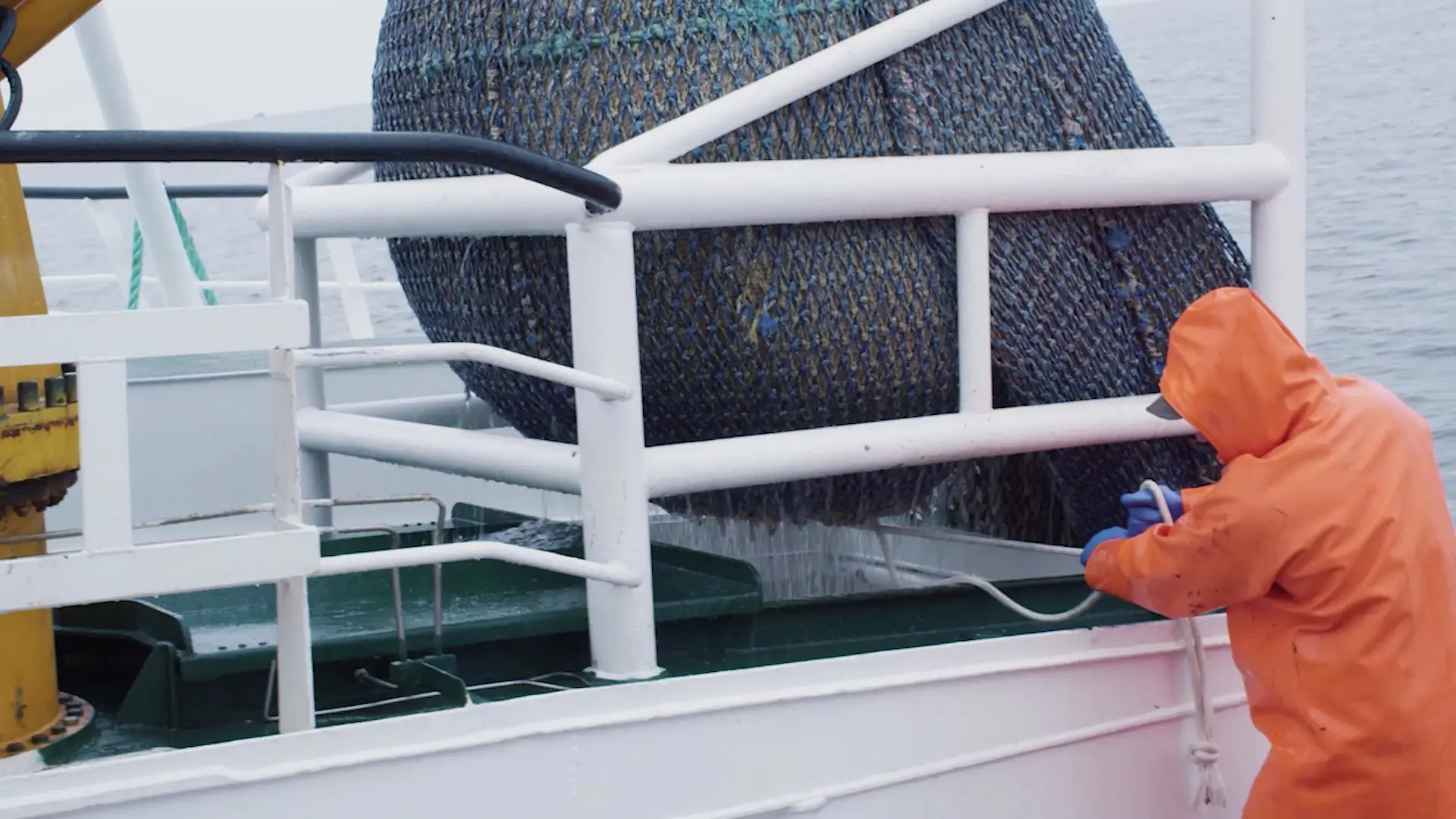 Fisherman in an orange suit working with the trawl net on deck